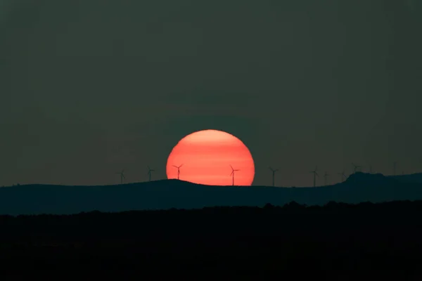 Huge orange sun at sunset with windmills — Stock Photo, Image