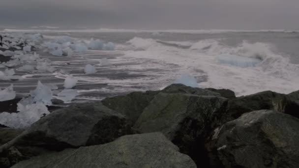 Волны ломаются медленно над огромными айсбергами на алмазном пляже с туристами — стоковое видео
