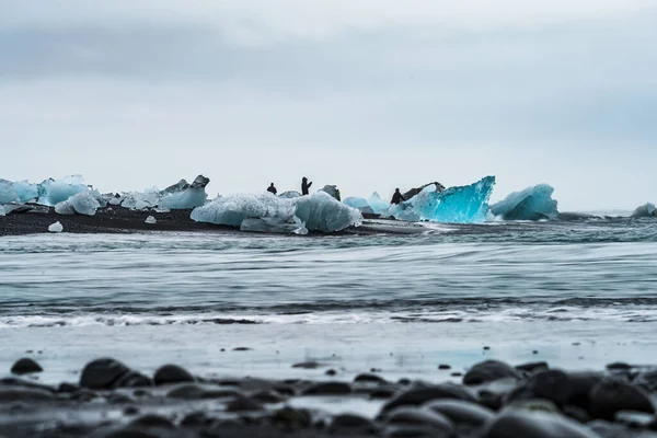 Blauwe ijsbergen over het zwarte zandstrand met toeristen — Stockfoto