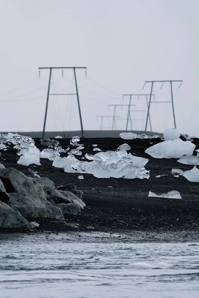 Zwart zandstrand en ijsberg diamanten met hoogspanningslijnen — Stockfoto