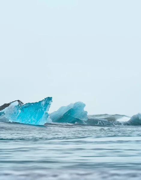 Icebergs azuis sobre a praia de areia preta sob o céu branco — Fotografia de Stock