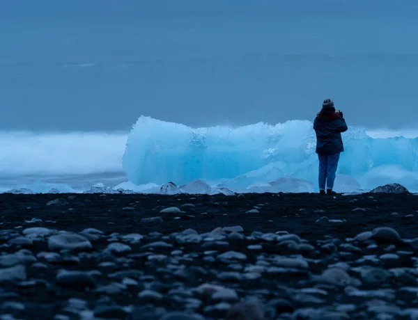 Blauwe ijsbergen over het zwarte zandstrand met toerist — Stockfoto