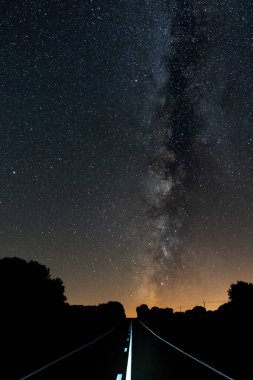 Samanyolunun altında beyaz çizgiler olan düz bir yol.