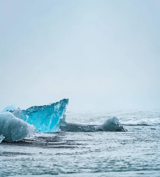 Djupblå isberg över den svarta sandstranden under vit himmel — Stockfoto