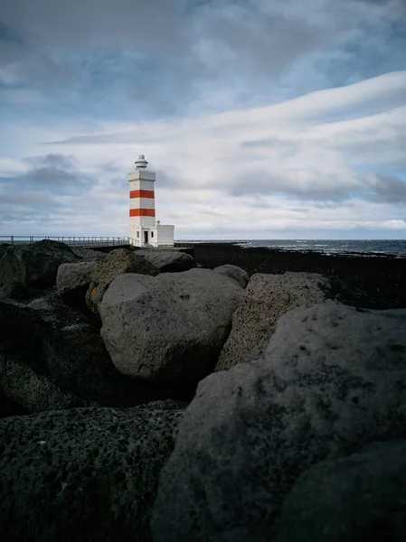 Lighthouse with red stripes wide angle over the black rocks — Foto Stock