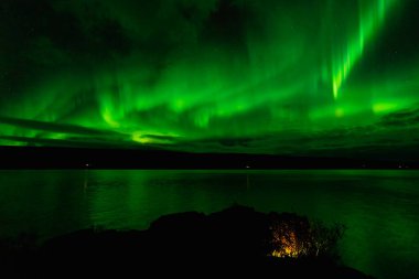 Gölün üzerinde yeşil yansımalı kuzey ışıkları