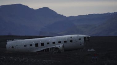 Arka planda uçak enkazı olan bulanık bir turist yürüyor.