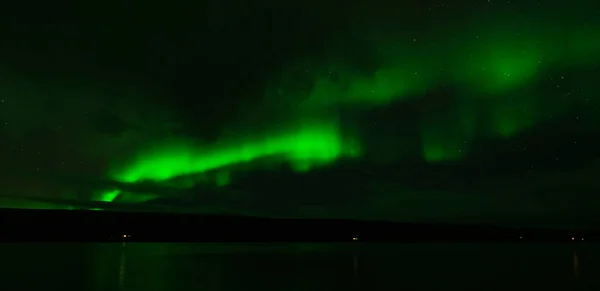 Northern lights over the calm lake with green lights
