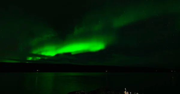 Northern lights over the calm lake with house lights