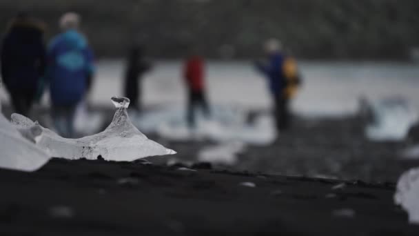 Eisberge Schwarzen Sandstrand Mit Verschwommenen Touristen Hintergrund Fokus Auf Eis — Stockvideo