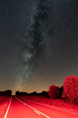 Samanyolunun altında beyaz çizgileri olan kırmızı yol, dikey bileşim