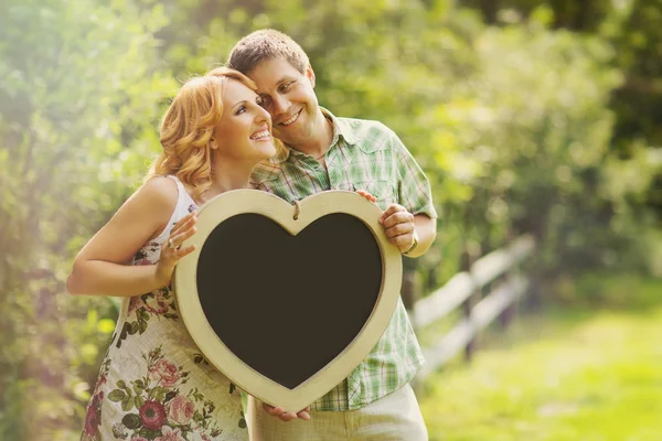 Couple holding heart shaped chalkboard — Stock Photo, Image