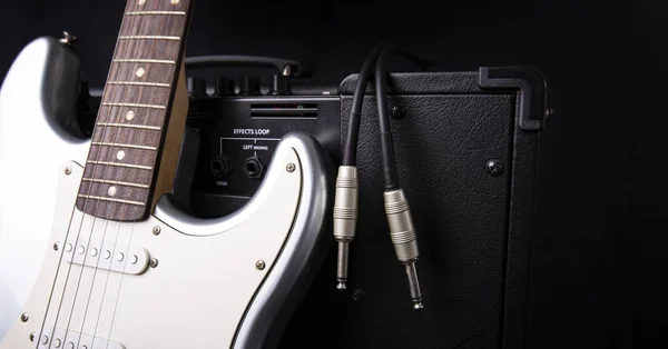 ホワイトを基調としたジャックケーブルとシルバーのエレキギターを備えたブラックギターアンプ — ストック写真