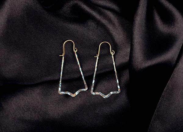 A metal earrings on black silk background — Zdjęcie stockowe