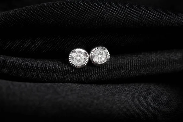 Round silver stud earrings with diamond on black fabric background — Stock Photo, Image