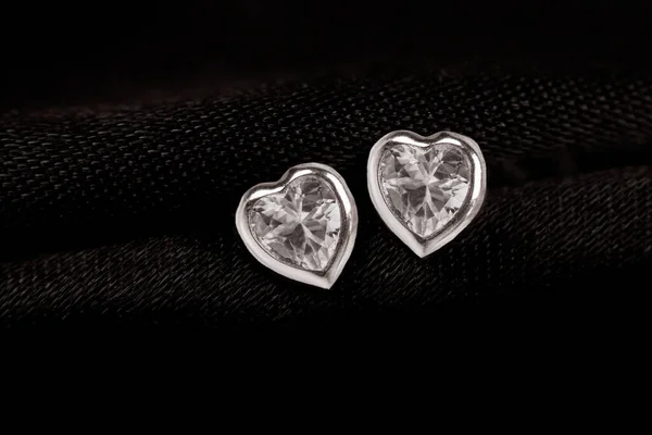Hearts-shaped silver stud earrings on black fabric background.. — Zdjęcie stockowe