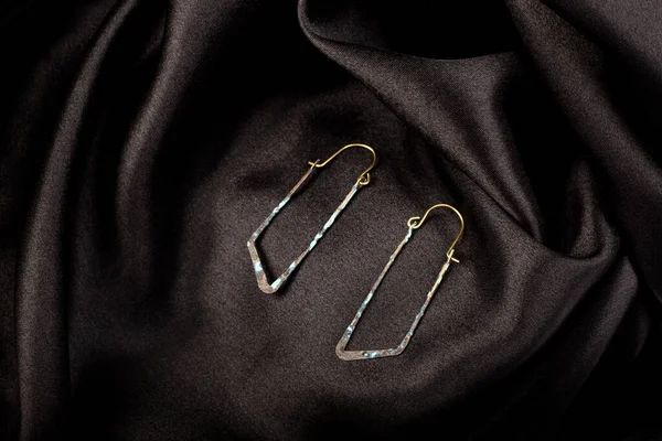 A metal earrings on black silk background — Zdjęcie stockowe