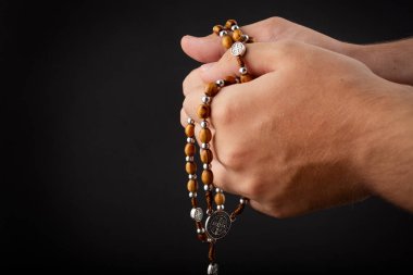 Siyah arka planda izole edilmiş dua sırasında elinde tespih tutan genç bir adamın elleri.