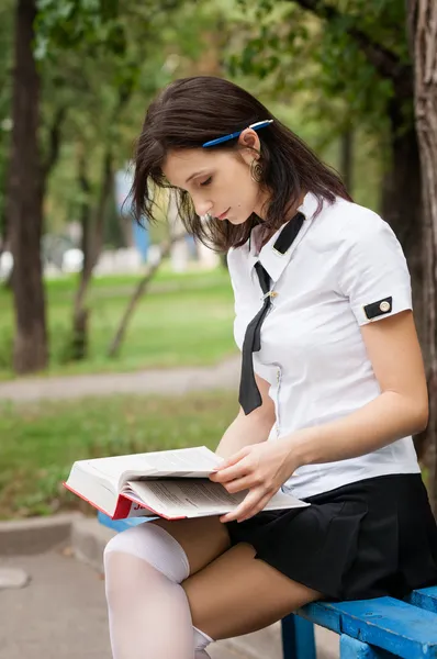 Dívka čtoucí knihu na ulici. školačka dělat své úkoly v parku. holka píše v poznámkovém bloku — Stock fotografie