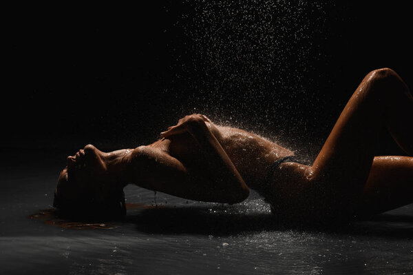Girl with a beautiful figure on a black cyclorama under the shower