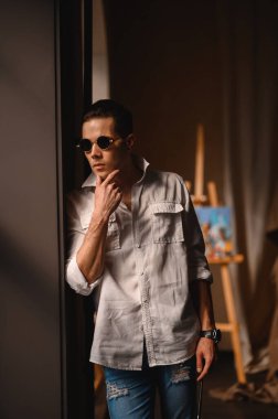 Şövalenin yanında gömlek ve güneş gözlüklü çekici bir esmer.