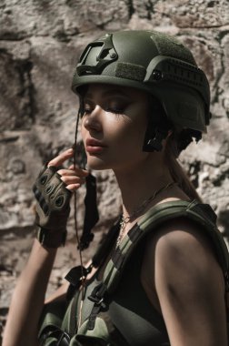 Military girl in uniform near a stone wall during the day. Portrait