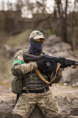 Soldier of the Armed Forces of Ukraine. A military man in tactical uniforms and with a machine gun in his hands sits on a stone