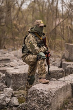 Ukrayna Silahlı Kuvvetleri 'nin askeri. Taktik üniformalı ve elinde makineli tüfekle bir taşın üzerinde oturan bir asker.