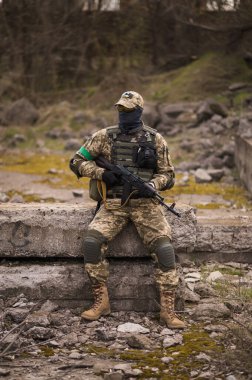 Soldier of the Armed Forces of Ukraine. A military man in tactical uniforms and with a machine gun in his hands sits on a stone