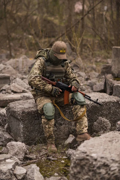 ウクライナ軍の兵士 戦術的な制服を着た軍の男と銃を手に石の上に座っている — ストック写真