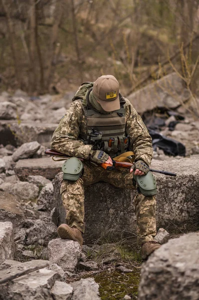 ウクライナ軍の兵士 戦術的な制服を着た軍の男と銃を手に石の上に座っている — ストック写真