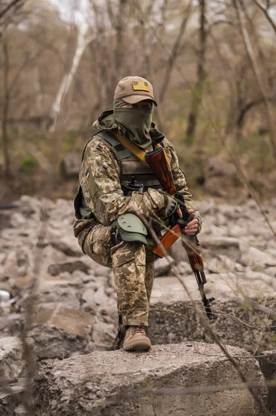 ウクライナ軍の兵士 戦術的な制服を着た軍の男と銃を手に石の上に座っている — ストック写真