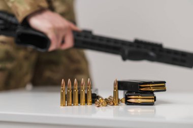 Bir asker masadan makineli tüfek alır. Beyaz bir masada fişekli makineli tüfek.