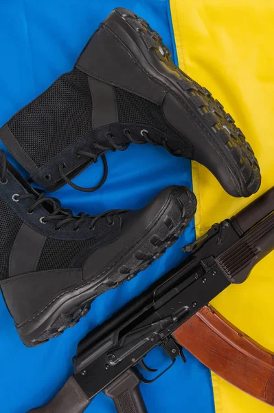 带有卡拉什尼科夫冲锋枪的皮革战术靴躺在乌克兰国旗上 — 图库照片