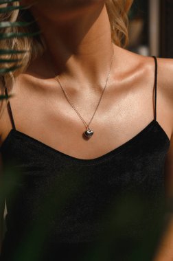 Güzel bir yaka zinciri ve kalp şeklinde bir kolyesi olan bir kız.