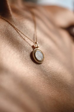 Genç bir kızın yakasında yuvarlak taşlı bir kolyeyle zincirlenmiş.