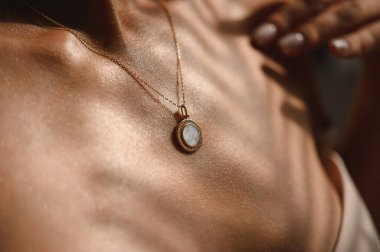 Genç bir kızın yakasında yuvarlak taşlı bir kolyeyle zincirlenmiş.