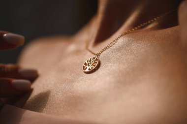 Genç bir kızın yakasında ağaç şeklinde bir kolye olan altın bir zincir.