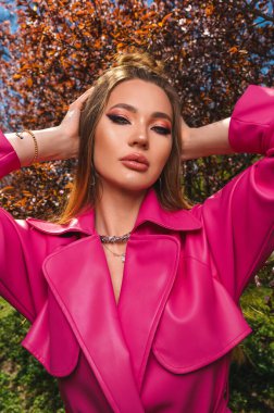 Çekici sarı saçlı Ukraynalı kız çiçek açan bahar ağaçlarında pembe deri ceketli.