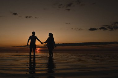 Okyanus kenarında günbatımının arka planında romantik bir çift. Gün batımı okyanus boyunca yürür