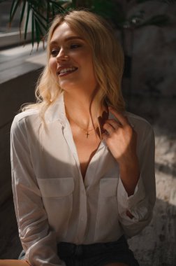 Beyaz ipek bluzlu narin ve şehvetli bir sarışın ve boynunda bir süslemeyle.