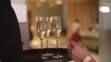 Garson tepsisinden bir bardak şampanya alan bir elin yakın çekimi.