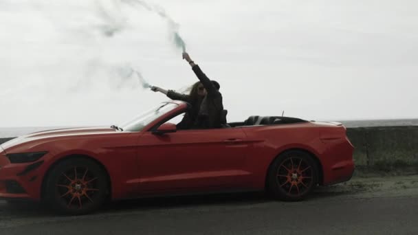 Paar in rotem Cabrio hält Kontrolleure mit farbigem Rauch in den Händen — Stockvideo