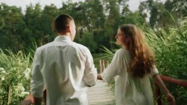 Genç ve mutlu bir çift ormanda nehir köprüsünde yürüyor.