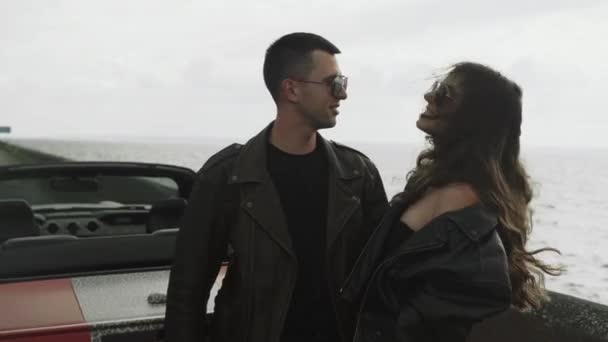 Молода пара стоїть біля моря і їх кабріолет — стокове відео