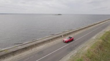 Nehir kenarındaki yolda kırmızı atlı spor araba, hava manzaralı.