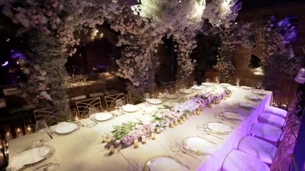 Restaurang hall dekorerad med blommor för bröllop. Bord med stolar i restaurang arrangerar för bröllopet. Tomma vinglas och tallrikar. Bra ställe med festlig atmosfär. — Stockvideo