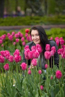 Güzel genç esmer, lalelerle çevrili parkta oturuyor.