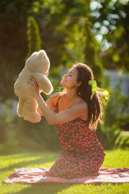 Genç bir kadın güneşli bir baharda oyuncak ayıyla oynuyor.