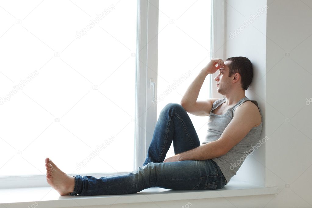 Handsome young man sitting on windowsill
